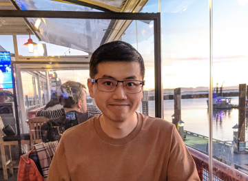 Dr. Kelvin Lou smiling at restaurant with the sun setting and boats on the water in the background.